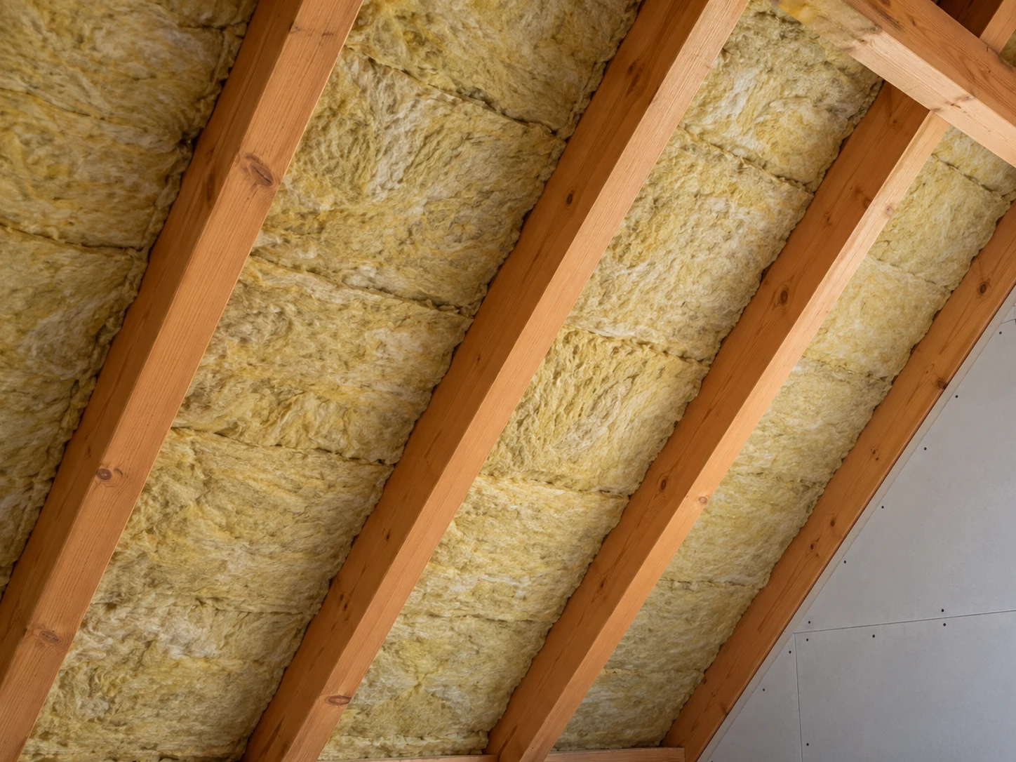 Mineralwolle zwischen Holzsparren einer Dachschräge während des Innenausbaus.