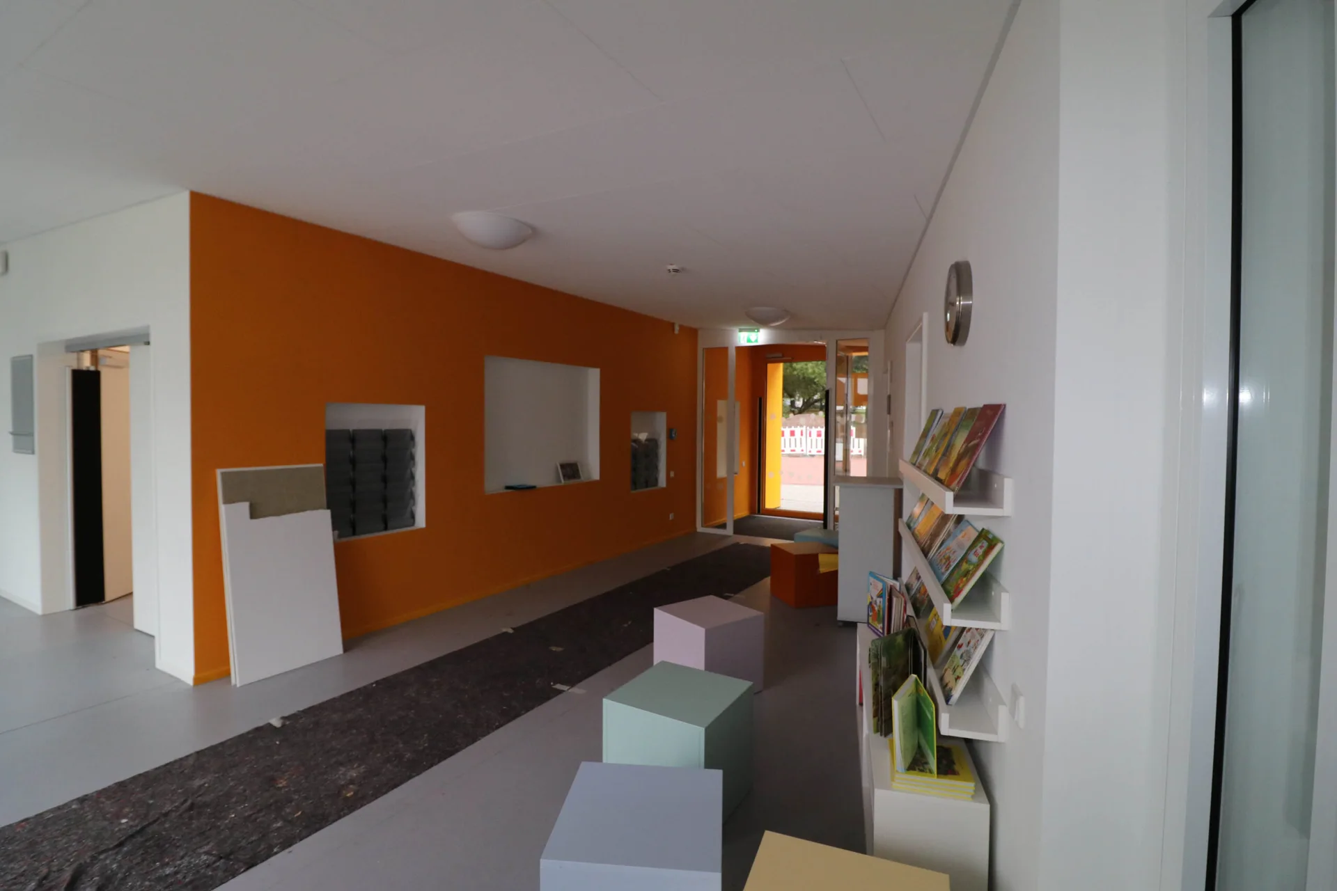 Helle Raumaufteilung mit orangefarbener Wand und integrierten Sitznischen im Familienzentrum Lysegang.