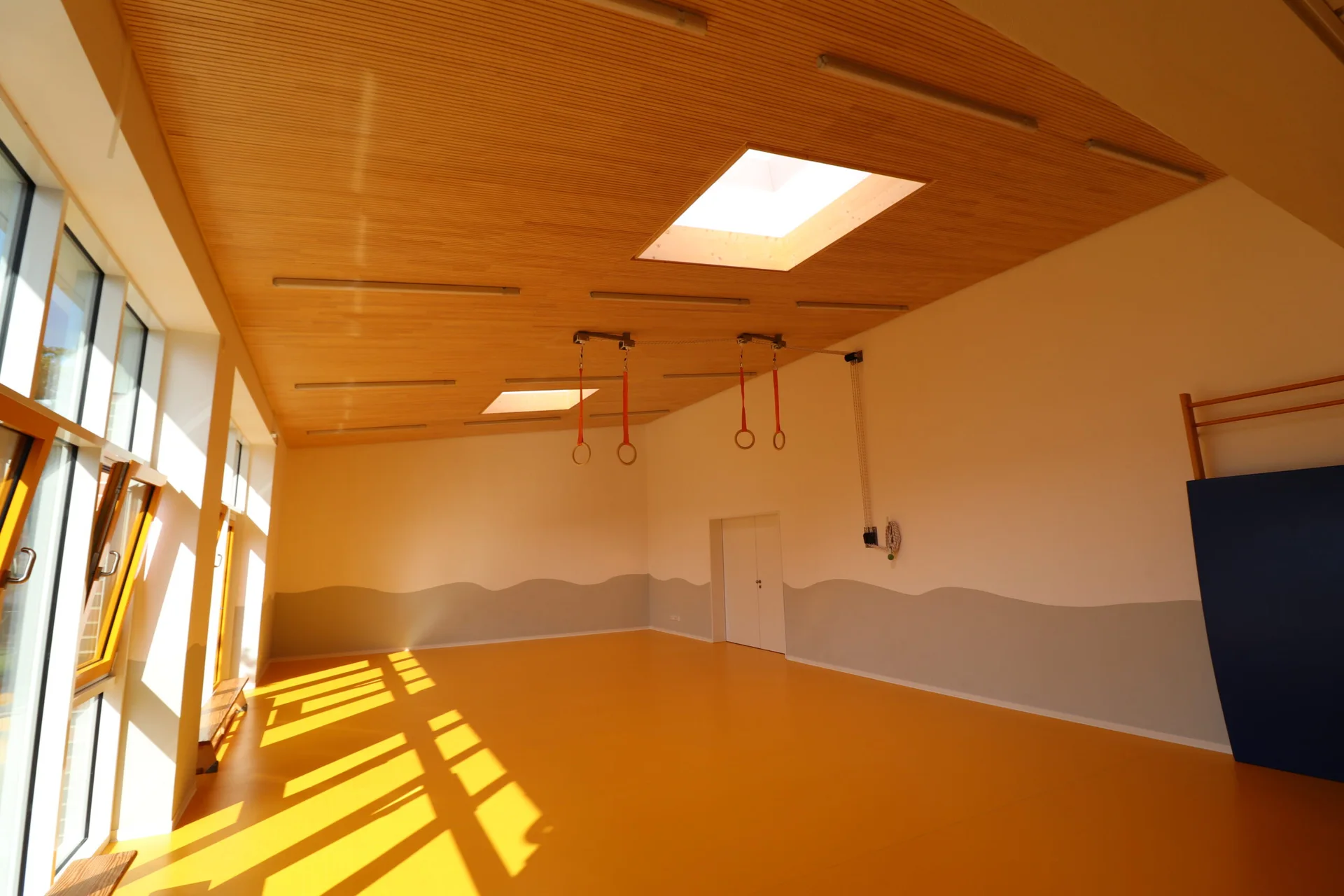 Holzdecke mit großen Oberlichtern und integrierten Leuchten im lichtdurchfluteten Bewegungsraum des Familienzentrums Wirbelwind.